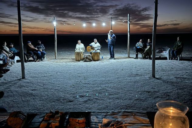 Cena en un living de campaña montado en medio del paisaje salino. Los visitantes comparten entrada, plato principal y postre acompañados por bebidas mientras el silencio del desierto envuelve la noche.