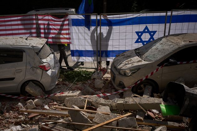 Las autoridades israelíes cuelgan banderas israelíes y estadounidenses en el sitio alcanzado por un misil iraní que mató a dos personas, en Ramat Gan, Israel, el miércoles 18 de marzo de 2026. (Foto AP/Oded Balilty)