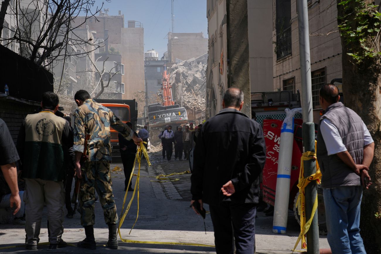 Transeúntes observan desde la distancia mientras los equipos de rescate y los socorristas trabajan en el lugar de un ataque que, según un funcionario de seguridad en la escena, destruyó la mitad de la Sinagoga Khorasaniha y edificios residenciales cercanos en Teherán, Irán, el martes 7 de abril de 2026. (Francisco Seco)