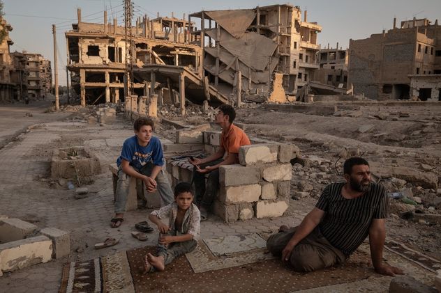 27- Abdelatif Daham Al Hummada (derecha) está sentado con sus hijos y su sobrino en la calle frente a su casa gravemente dañada, en Deir al-Zour, Siria.