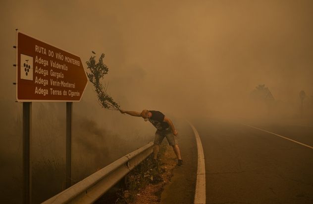 14- Un hombre combate un incendio con una rama en Cualedro (Ourense, Galicia). Ante la escasez de recursos, vecinos usan ramas, herramientas y mangueras para apagar las llamas.