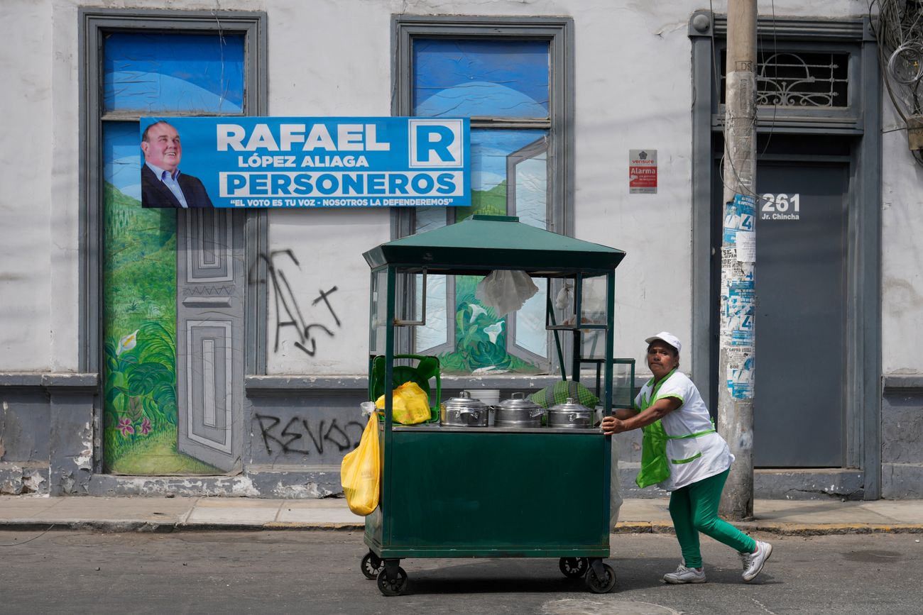 Una vendedora de tratamientos humectantes empuja su carrito junto a un cartel de campaña que promueve al candidato presidencial Rafael López Aliaga, exhibido en un edificio que está al lado de la Oficina Nacional de Procesos Electorales mientras continúa el conteo de votos tres días después de las elecciones generales, en Lima, Perú, jueves 16 de abril de 2026. (Martin Mejia)