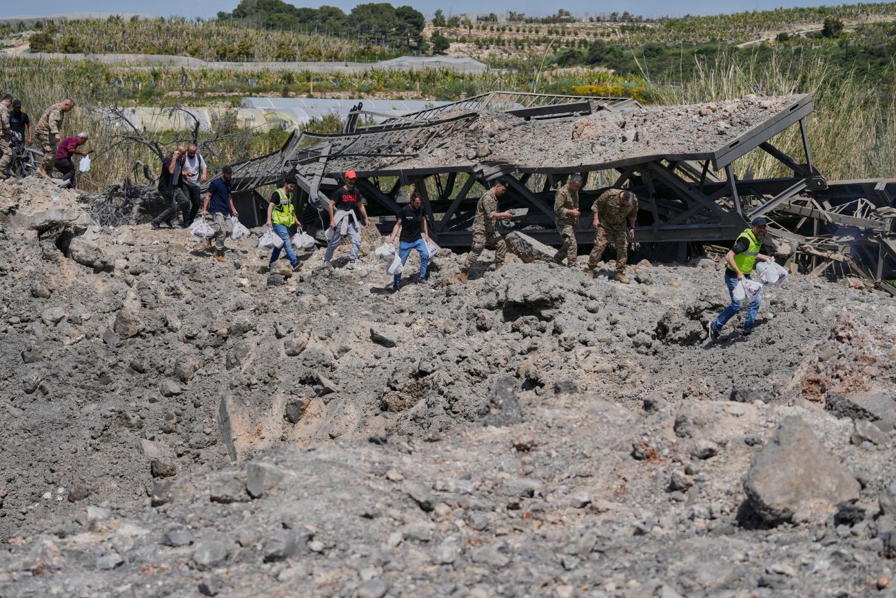 Soldados y civiles libaneses cruzan a pie un cráter tras un ataque aéreo israelí que destruyó el puente Qasmiyeh cerca de la ciudad costera de Tiro, Líbano, el jueves 16 de abril de 2026. 