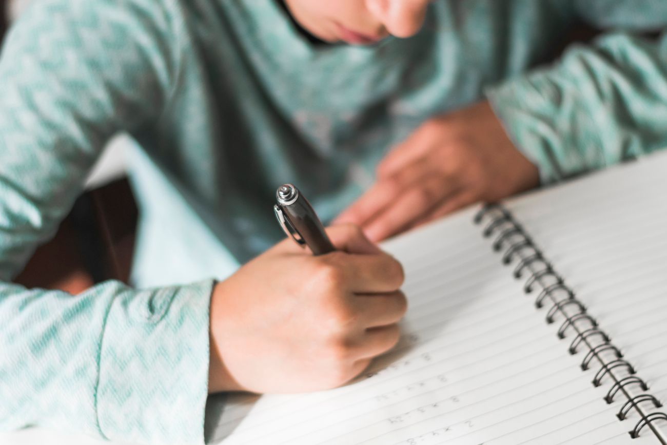 Alumno escribiendo a mano en su carpeta.