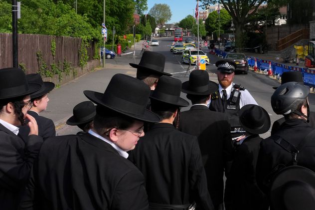 Un grupo de judíos ortodoxos observa la calle custodiada donde fueron apuñalados dos miembros de la comunidad, en Golders Green, Londres. 