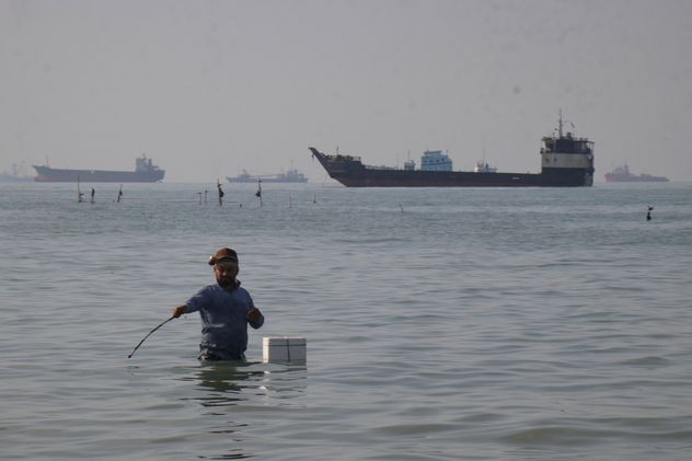 Un hombre está de pie en el agua mientras portacontenedores, barcos de carga y embarcaciones de servicio se alinean en el horizonte en el Estrecho de Ormuz frente a Bandar Abbas, Irán, el 27 de abril de 2026. (Razieh Poudat)