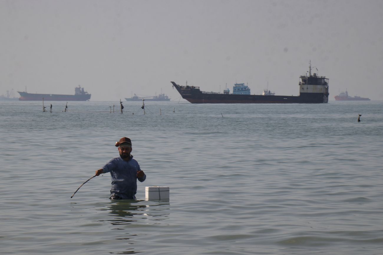 Un hombre pesca con su caña a orillas del estrecho de Ormuz. Al fondo, los petroleros comienzan a moverse al anunciarse el acuerdo.