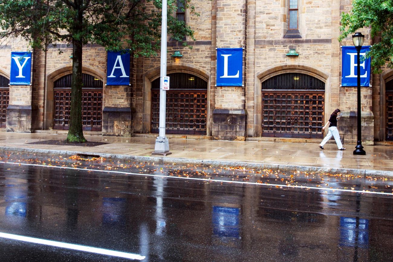 Una mujer camina junto a un letrero de Yale reflejado en el agua de lluvia en el campus de la Universidad de Yale en New Haven, Connecticut, el 22 de agosto de 2021. (Foto AP / Ted Shaffrey / Archivo)