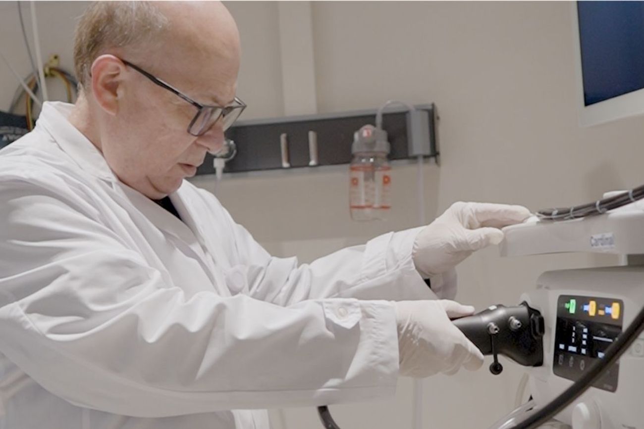Médico especialista con bata blanca y guantes quirúrgicos ajustando el instrumental de una torre de endoscopía digital en un quirófano. 