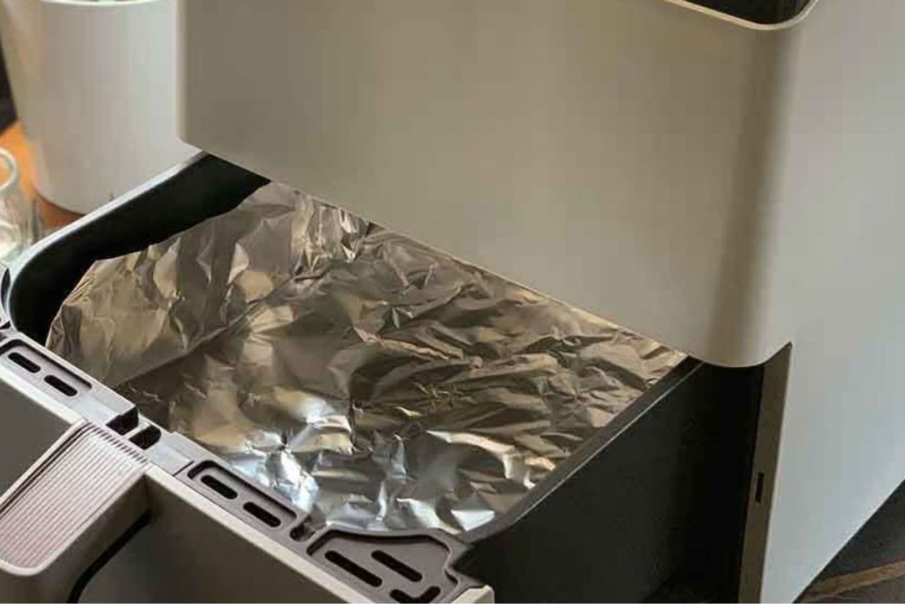 El papel aluminio puede ayudar a recoger grasa y residuos, facilitando la limpieza de la freidora de aire.