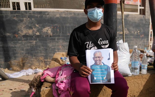 Kevin Tovar está sentado cerca de su casa dañada sosteniendo folletos con una foto de su padre desaparecido en La Guairá, Venezuela, el 26 de junio de 2026, dos días después de que los terremotos gemelos azotaran el país. (Ariana Cubillos)