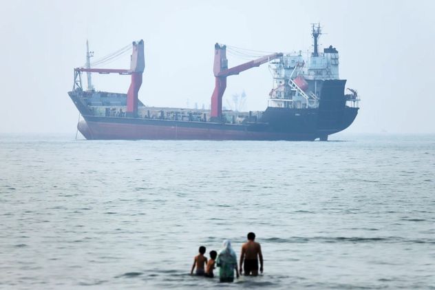 Un grupo de personas se encuentra en aguas poco profundas mientras un barco de carga parece anclado en el Estrecho de Ormuz frente a Bandar Abbas, Irán, el 30 de junio de 2026. (Amirhosein Khorgooi)