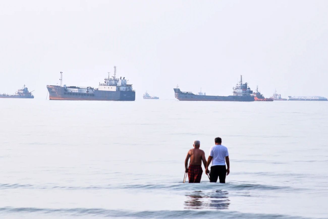Dos hombres vadean en las aguas del Estrecho de Ormuz con embarcaciones ancladas al fondo, frente a Bandar Abbas, Irán, el 12 de julio de 2026. (Razieh Poudat)