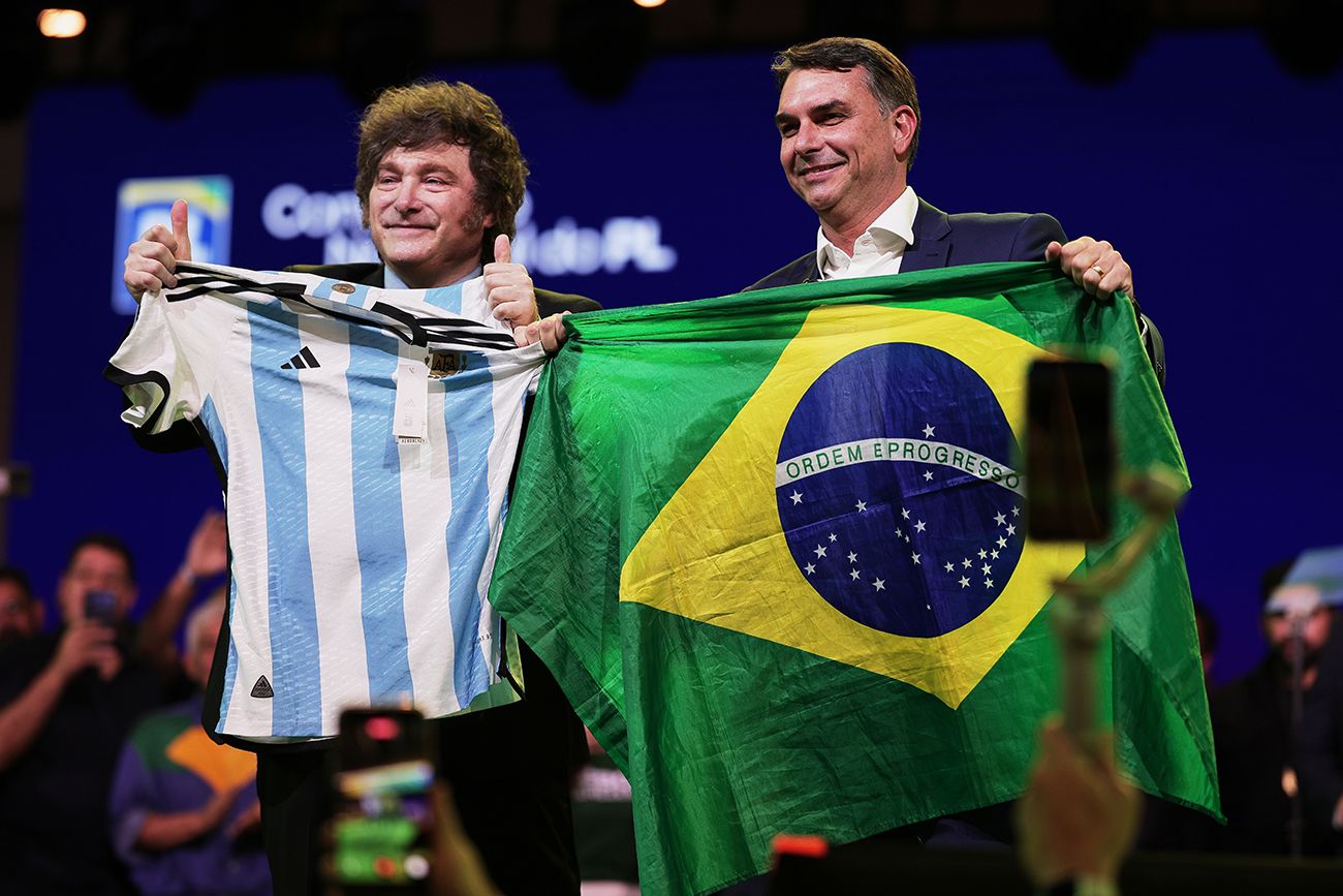 El senador brasileño Flavio Bolsonaro sostiene una bandera de Brasil mientras el presidente argentino Javier Milei hace lo propio con una camiseta de la selección argentina de fútbol, durante la convención del Partido Liberal, en la que se confirmó a Bolsonaro para que sea el candidato presidencial del partido.