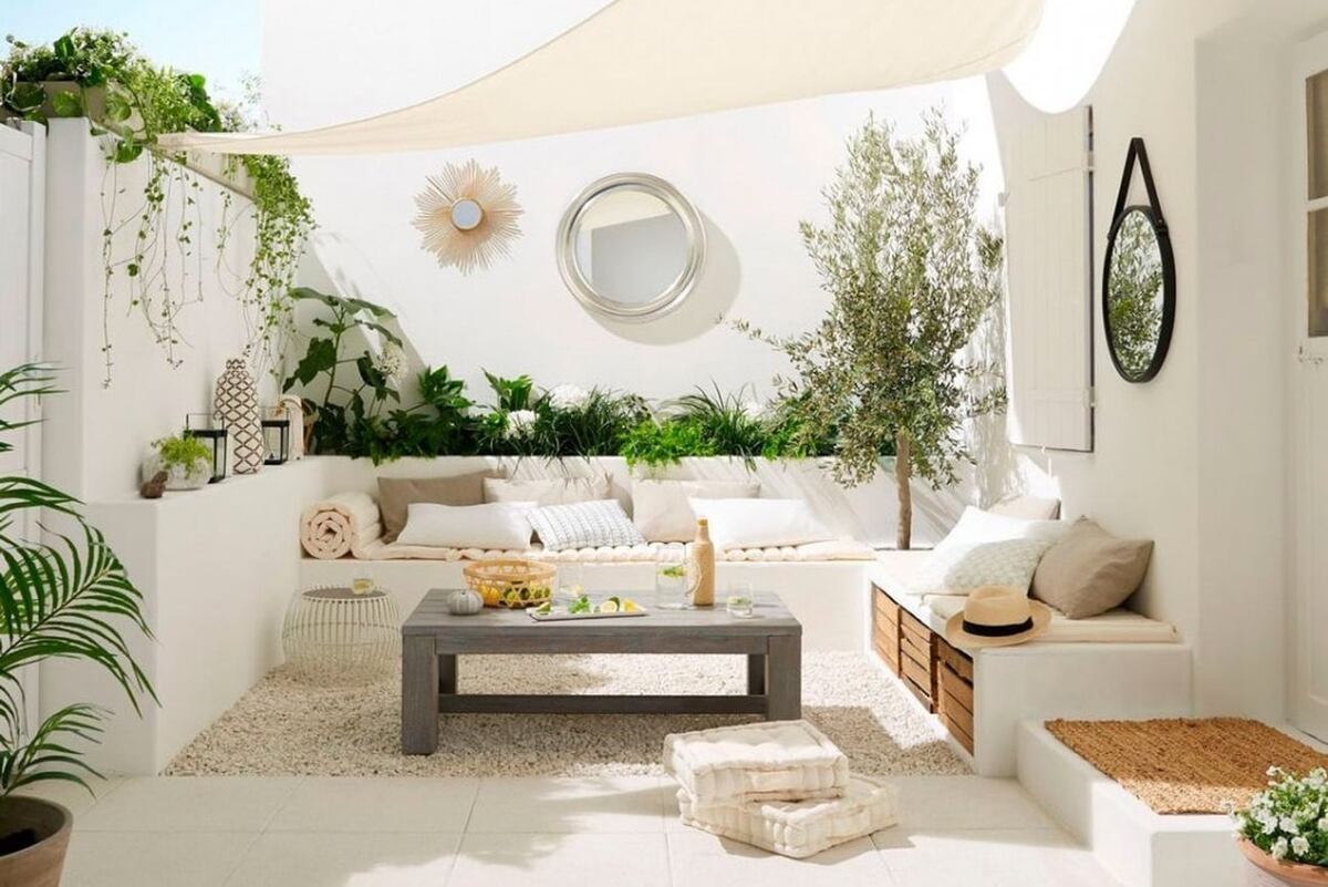 En un patio pequeño con piso claro resaltan la madera, los textiles, el verde de las plantas y los objetos de decoración para generar un ambiente relajado y chill. Foto: Pinterest
