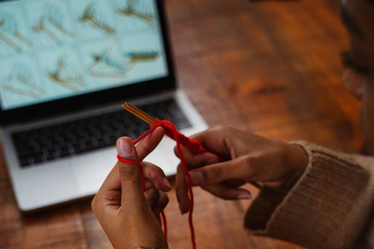 Mujer haciendo crochet mientras se guia de la computadora