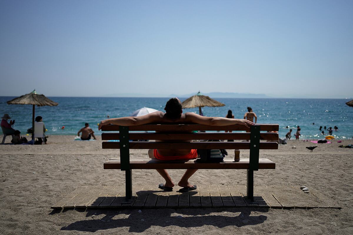 Un hombre toma el sol sentado en un banco durante una ola de calor en la playa pública de Paleo Faliro, en el sur de Atenas, Grecia, el lunes 21 de julio de 2025. (Foto AP/Thanassis Stavrakis)