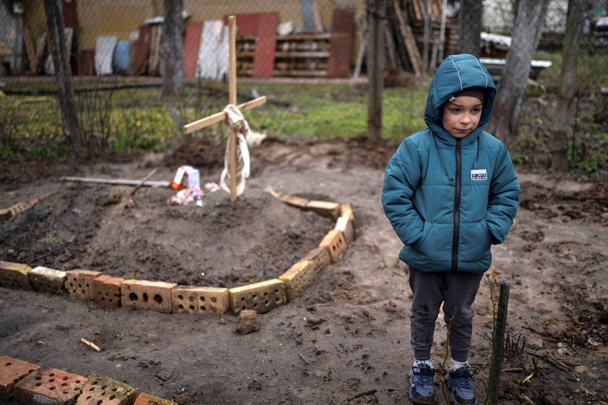 En el patio de su casa, Vlad Tanyuk, de 6 años, se encuentra cerca de la tumba de su madre Ira Tanyuk, quien murió de hambre y estrés debido a la guerra, en las afueras de Kiev, Ucrania, el lunes 4 de abril de 2022. (AP)