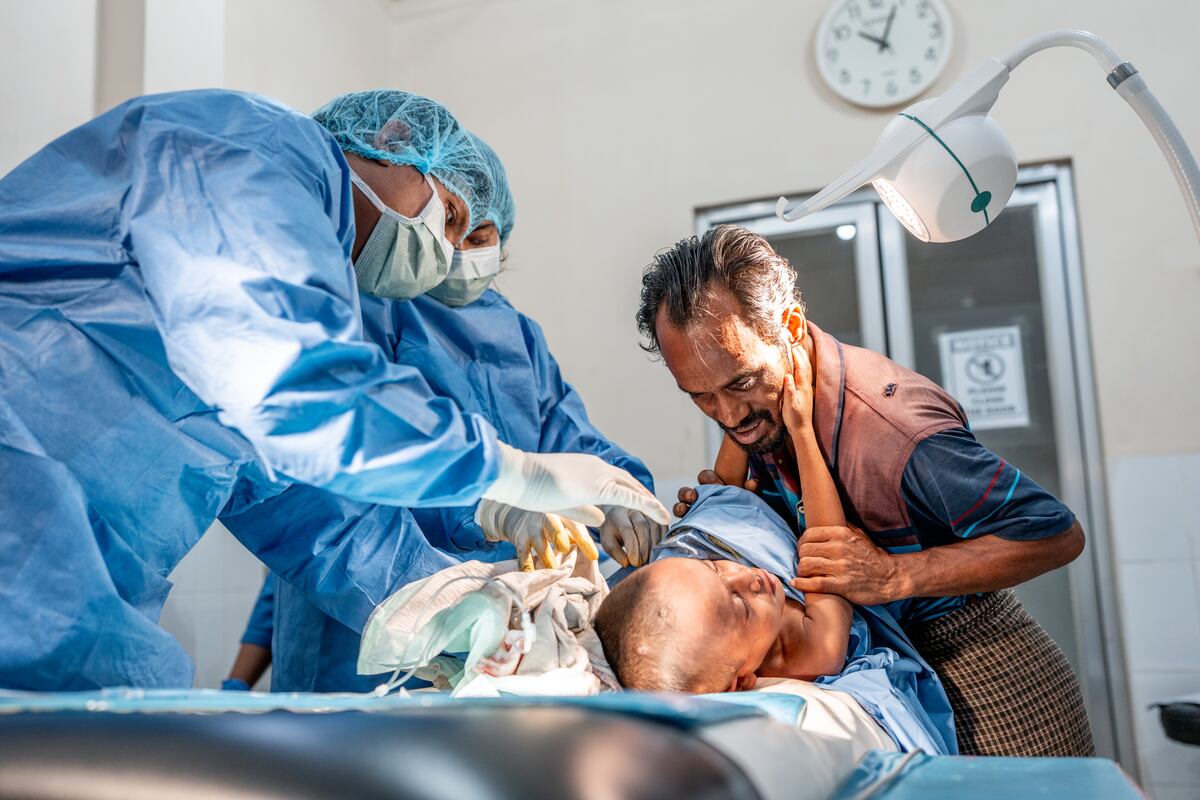 Shofi Mohammad recibe tratamiento por abscesos en la sala de emergencias del hospital de MSF en Kutupalong. Mientras la doctora Hasna Hena Mou y el asistente médico Rajib Mazumdar realizan una incisión y drenaje, el padre de Shofi, Anas Mohammad, intenta consolarlo. Cox’s Bazar, Bangladés. (Ante Bussmann/MSF)