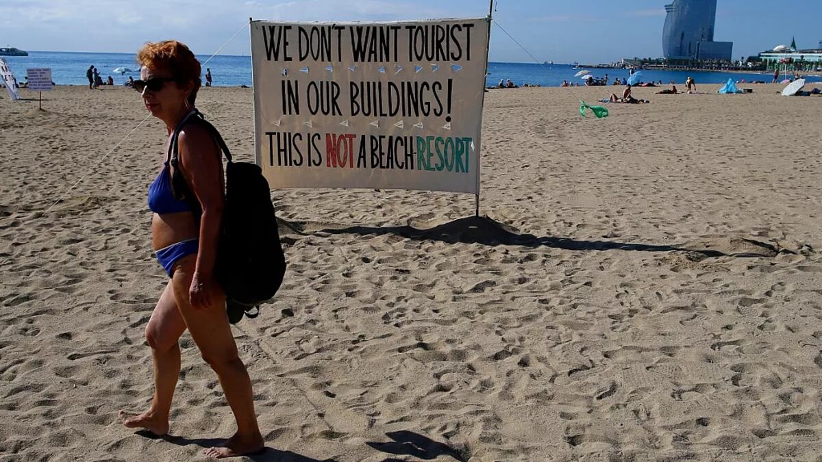 Una mujer camina frente a una señal que reza '¡No queremos turistas en nuestros edificios! Esto no es un resort de playa (Foto: AP Photo/Manu Fernandez)