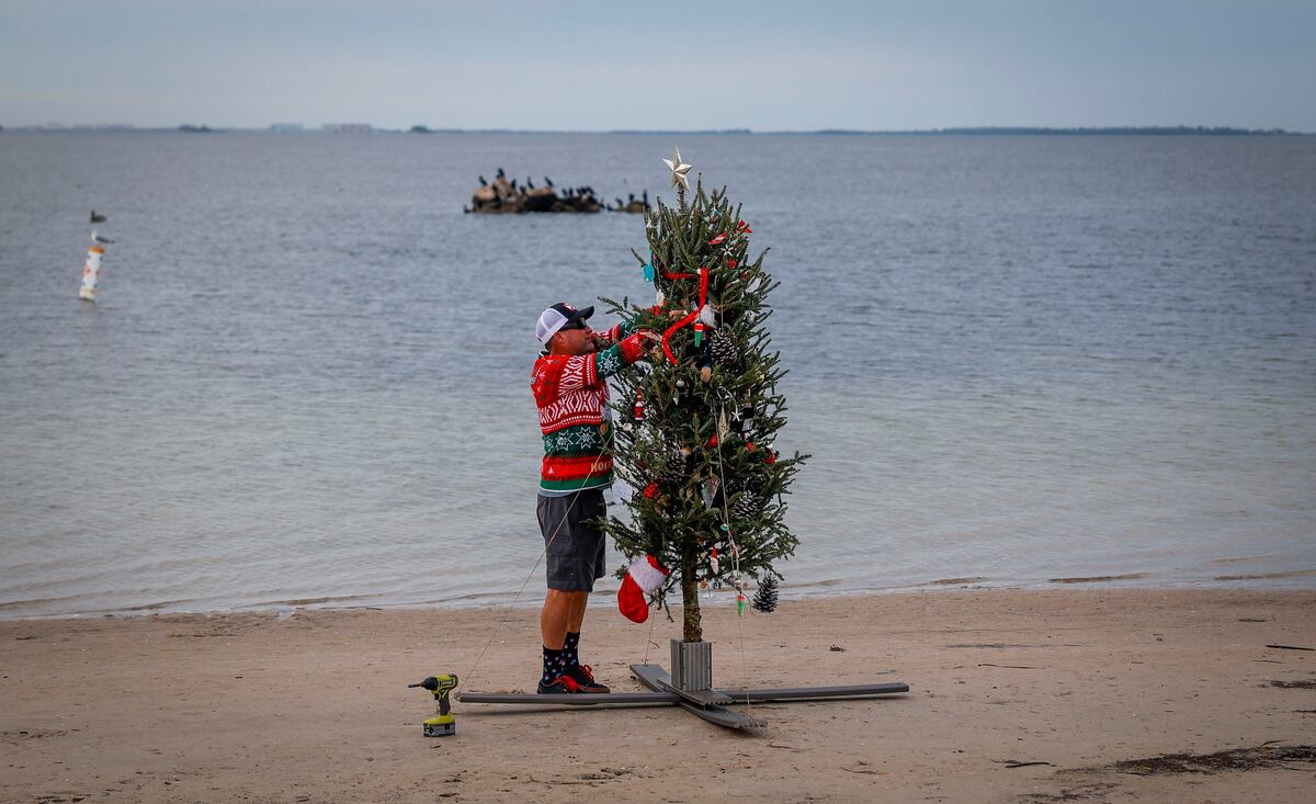 Mike Womack, de 52 años, le da los toques finales a un árbol de Navidad a lo largo de Sunset Beach el domingo 24 de diciembre de 2023 en Tarpon Springs, Florida. Durante los últimos nueve años, Womack ha instalado un árbol a lo largo de la playa para que lo disfruten los residentes locales. (Chris Urso/Tampa Bay Times vía AP)
