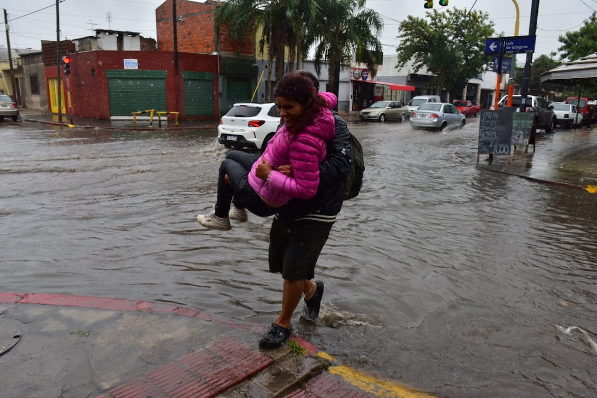 En medio de la lluvia de este viernes en Córdoba, David cruza a Pamela en brazos en la esquina de Saavedra y Góngora. (José Hernández/La Voz)