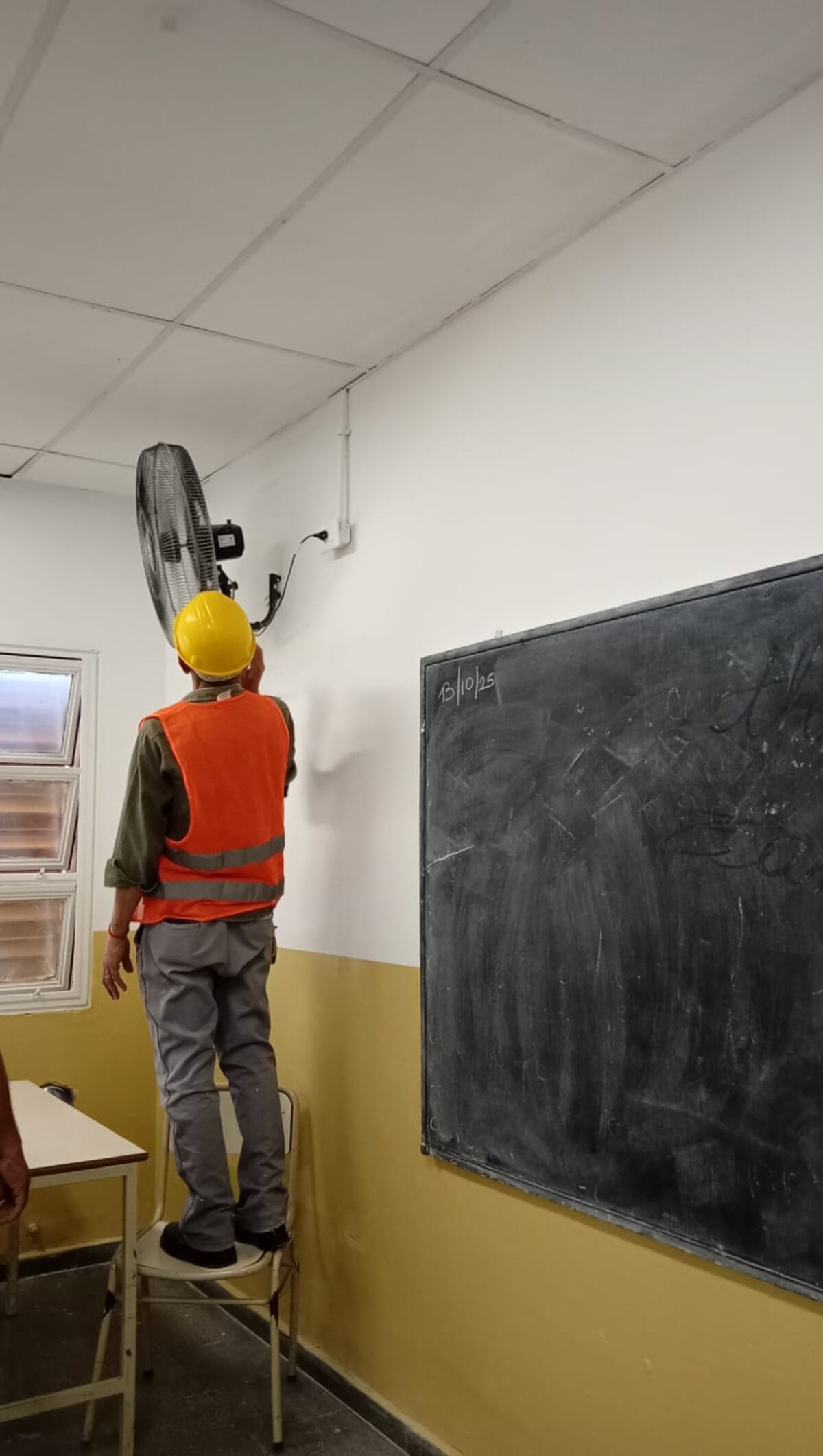 Operario instala un ventilador de pared en una escuela de Córdoba.