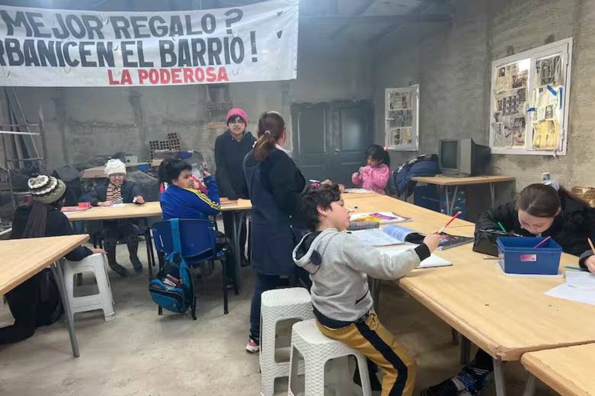 Santino y otros vecinos del barrio participan del apoyo escolar y de la merienda; el principal reclamo queda plasmado en el cartel: que urbanicen el barrio. Foto: La Nación