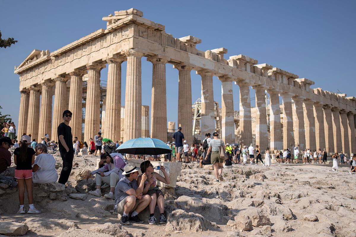 Una turista bebe agua mientras ella y un hombre se sientan bajo una sombrilla frente al templo del Partenón, del siglo V a. C., en la colina de la Acrópolis, durante una ola de calor, el 13 de julio de 2023. (Foto AP/Petros Giannakouris, Archivo)